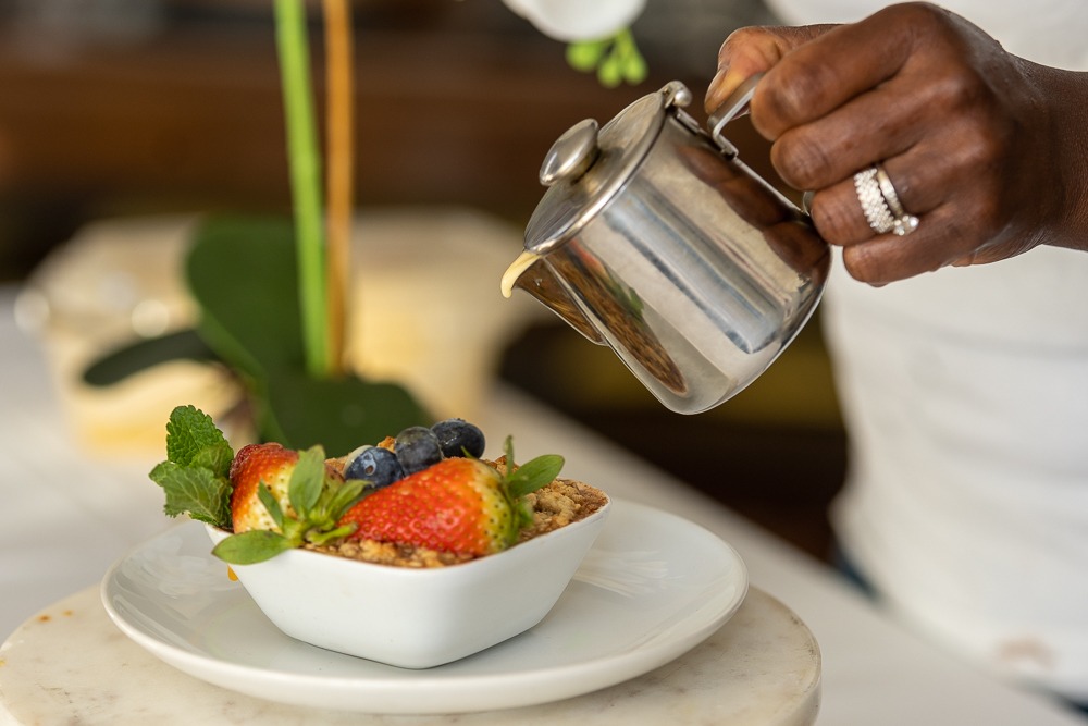 Chef pouring cream sauce over beautifully presented fruit crumble — Sisi Olonje attention to detail