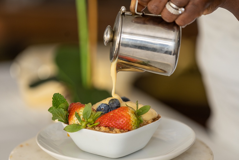 Chef pouring custard over a beautifully presented fruit crumble dessert