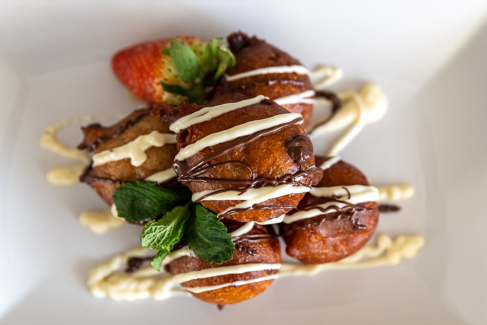 Large puff puff pieces with chocolate and white sauce drizzle from above
